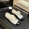 Chanel two-tone ivory and black leather ballet flats with gold CC logo, Mary Jane strap, displayed on black surface with Chanel box in background