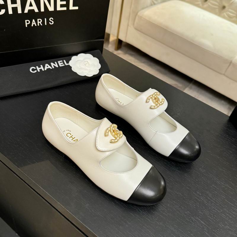 Chanel two-tone ivory and black leather ballet flats with gold CC logo, Mary Jane strap, displayed on black surface with Chanel box in background